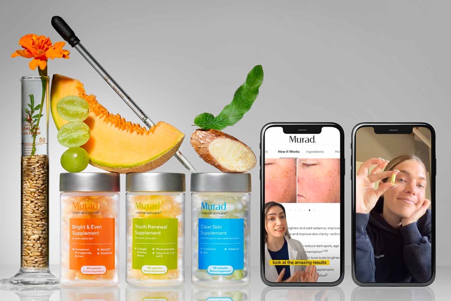 Murad products with pomegranate and papaya stacked on it, next to a vase with an orange flower in it and a pipette leaning across it