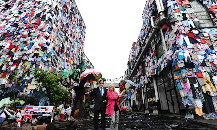 Joanna Lumley standing in front of street if buildings covered with the 3.6 million items of clothes that people have 'shwopped'