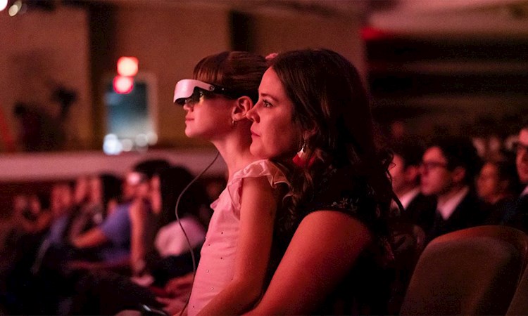 Girl sat on her Mother's knee watching the ballet with Dell's eSight glasses on