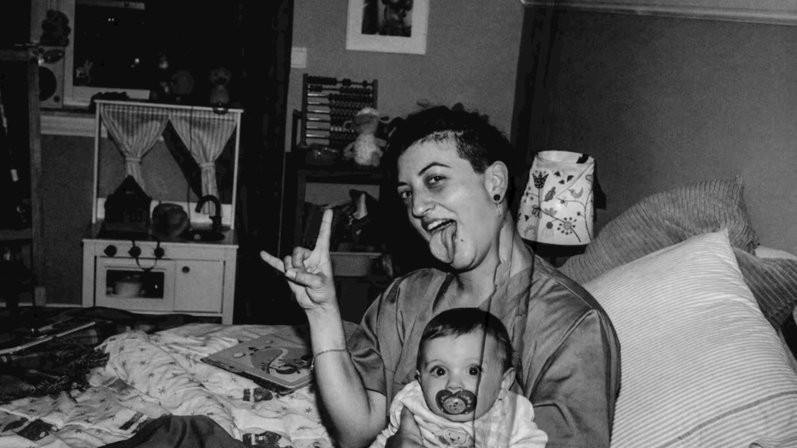Mother making a rock sign holding a baby on a bed