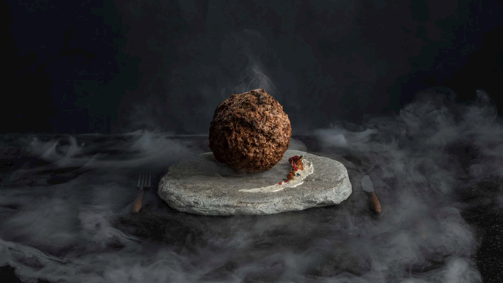 A large meatball made of mammoth meat on a stone platter in a dark studio set with mist swirling around it