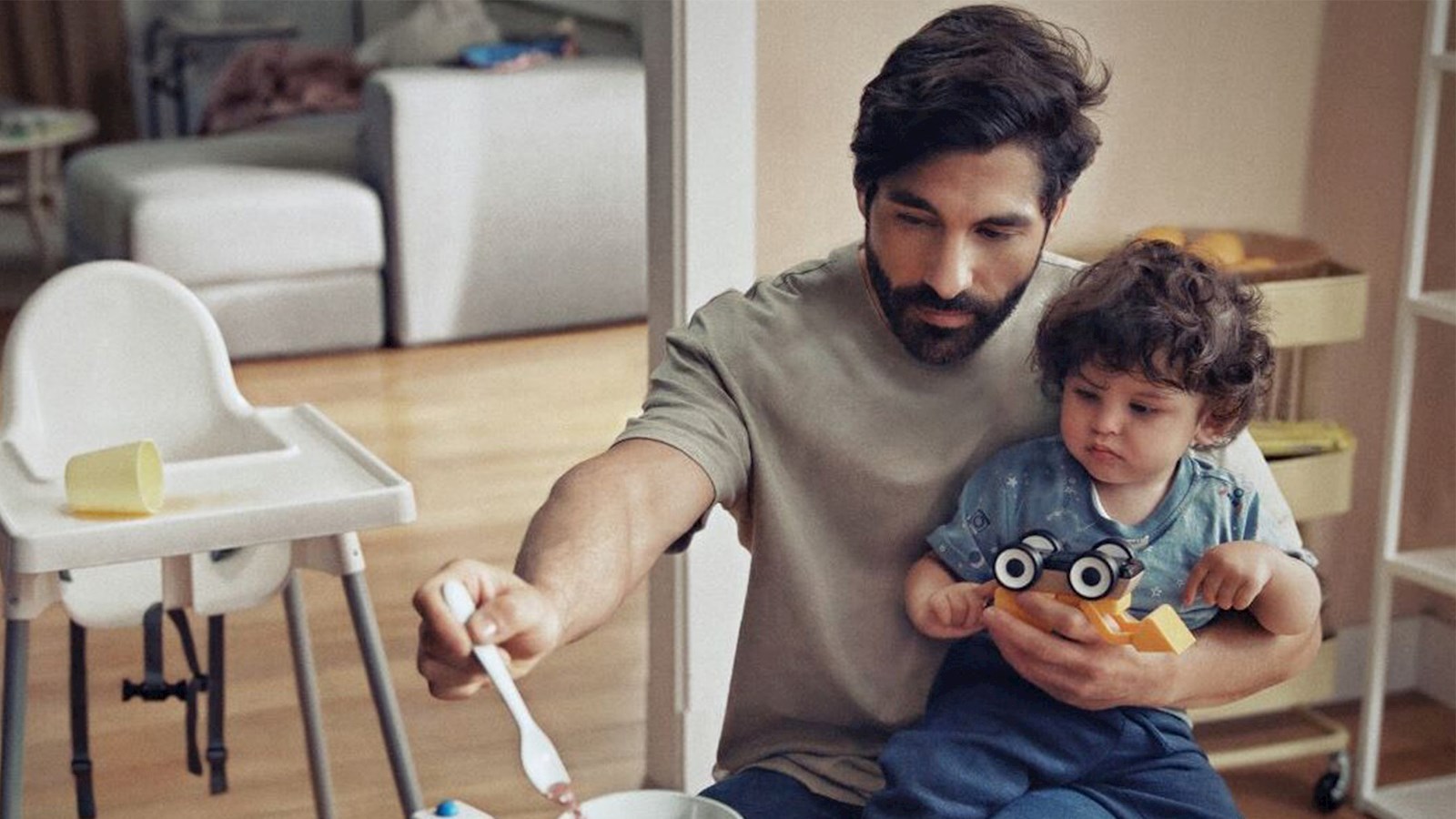 Man feeding a baby with IKEA ANTILOP highchair in background
