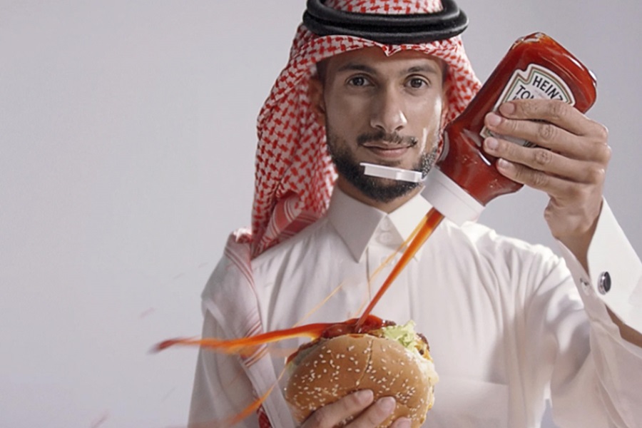 Man dressed in a thobe squirting Ketchup onto a burger