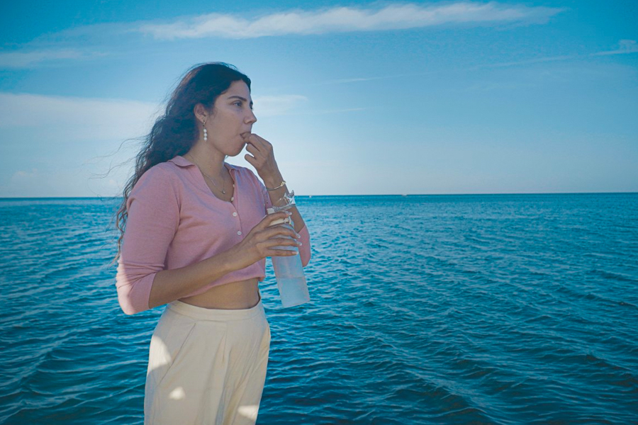 Woman standing with sea in the background taking a pill