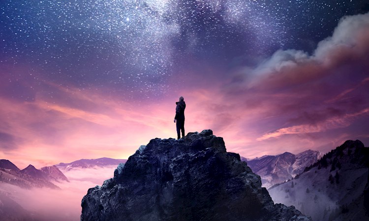 Person on top of a mountain looking up at the stars 
