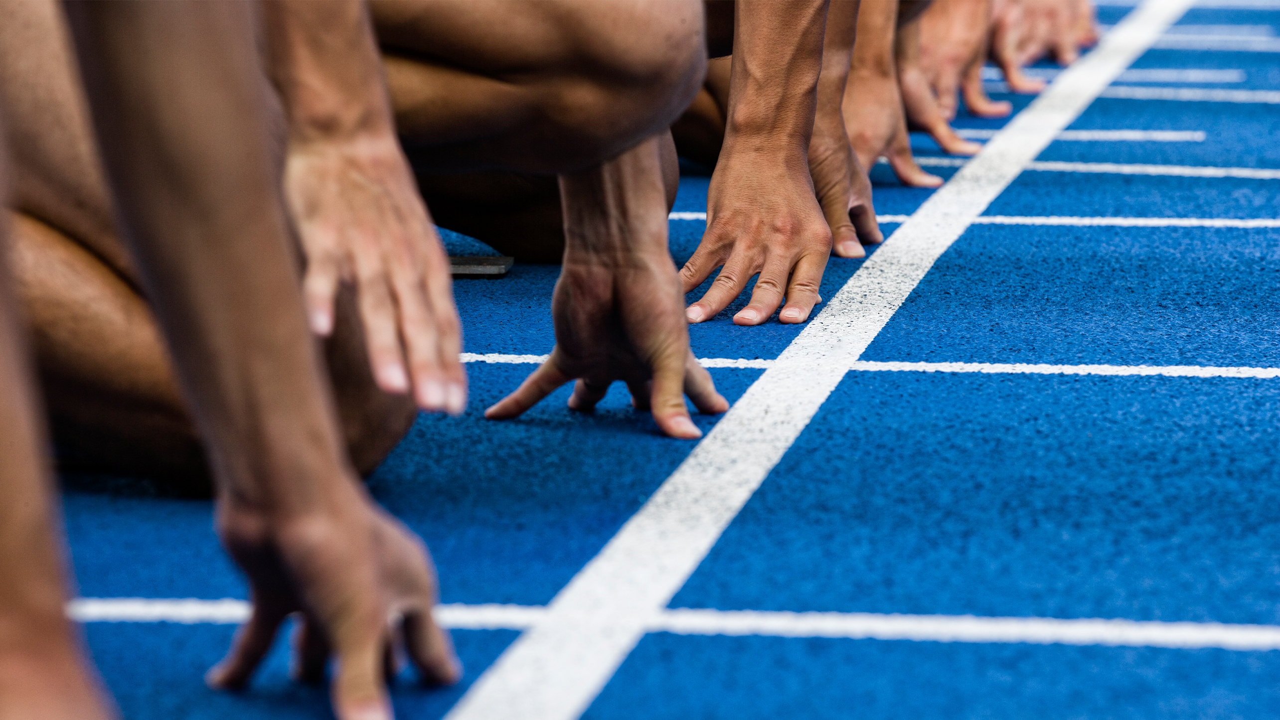 Close up of the hands of people lining up at the start line of an athletics track