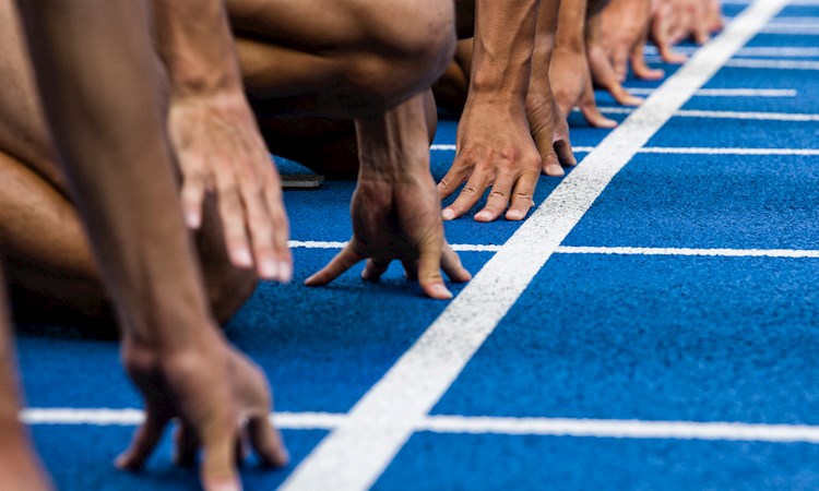 Close up of the hands of people lining up at the start line of an athletics track