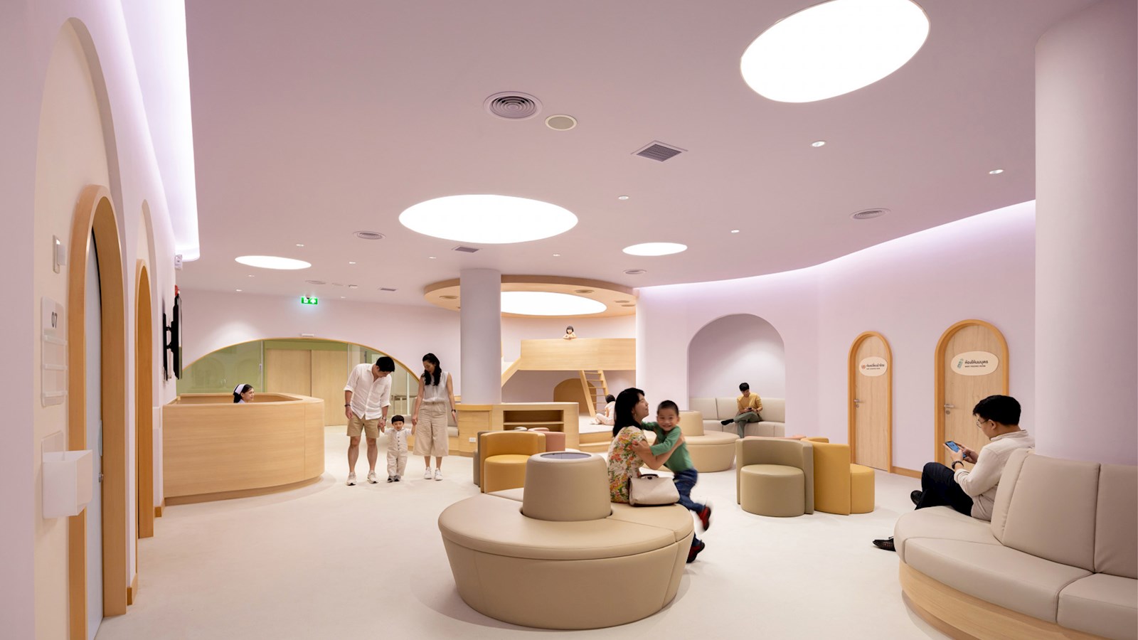 Waiting room of children's hospital, featuring parents and children in pastel pink room with modern furniture