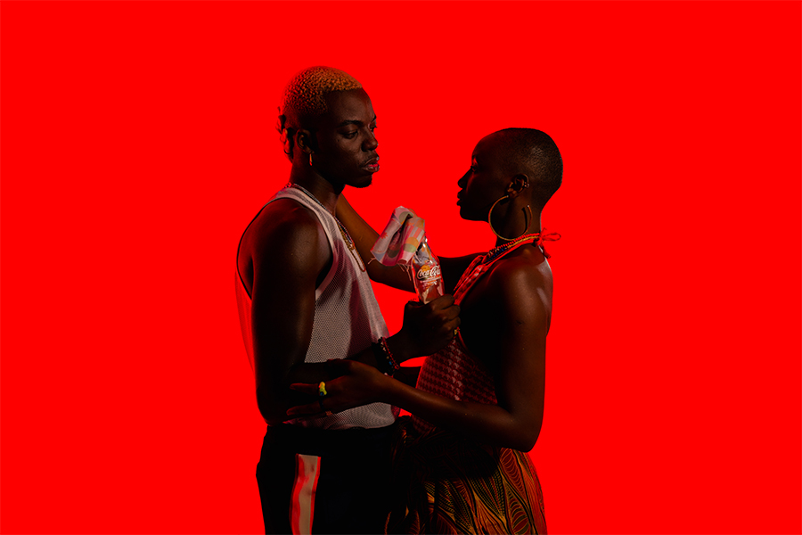 Two people holding a bottle of Coca-Cola between them on bright red background 