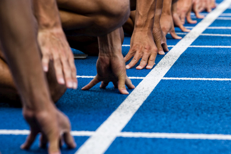 Runners' hands at starting line on a blue running track