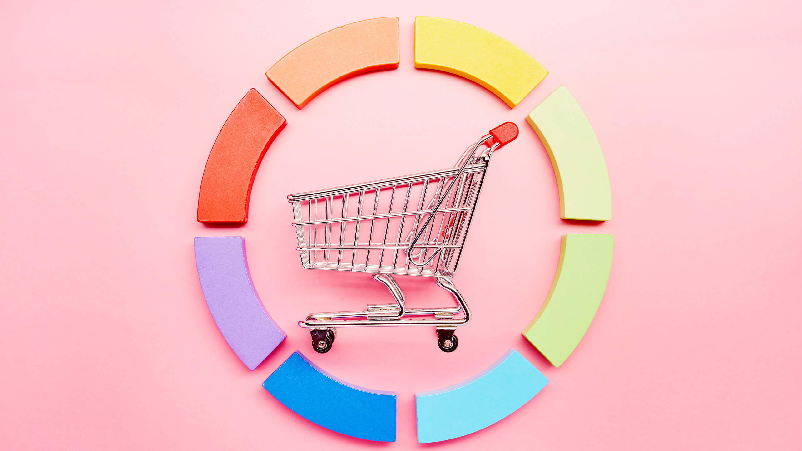 Pie chart made of colourful building blocks and a small shopping cart on pink background