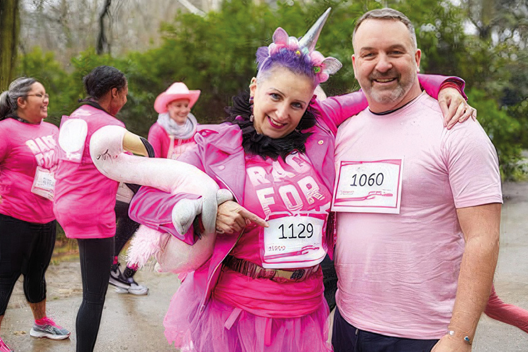 A woman dressed in pink holding a flamingo, wearing a unicorn horn and man dressed in pink and smiling